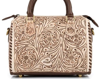 May include: A cream-colored handbag with a brown handle and accents. The bag features a detailed floral pattern carved into the leather. The bag has a top handle and small feet. The bag is approximately 10 inches wide.