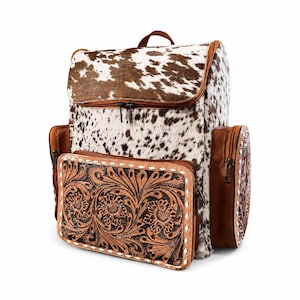 May include: A backpack featuring a brown and white cowhide pattern on the main body and top flap. The front and side pockets are made of brown leather with intricate floral tooling and white whipstitch detailing along the edges and zippers.