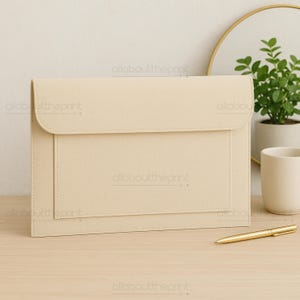 May include: A beige leatherette document holder with a flap closure and a stitched border. The holder has a rectangular pocket on the front and is sitting on a light wood surface. A gold pen is next to the holder.