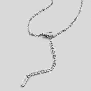 K&ouml;nnte beinhalten: Eine silberfarbene Halskette mit einer filigranen Kette und einem Karabinerverschluss. Die Halskette hat eine Verl&auml;ngerungskette mit einem kleinen rechteckigen Anh&auml;nger mit der Aufschrift "S.HENTS". Der Schmuck wird vor einem hellgrauen Hintergrund pr&auml;sentiert.