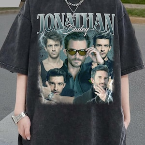 May include: Dark gray t-shirt featuring a collage of images of Jonathan Bailey. The shirt has a vintage, distressed look with the name "Jonathan Bailey" in a stylized font. The shirt is a short-sleeved, oversized fit.