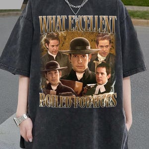 Puede incluir: Camiseta gris oscuro con un diseño vintage. El gráfico muestra el texto "WHAT EXCELLENT BOILED POTATOES" y un collage de hombres con trajes. La camiseta tiene un aspecto ligeramente desgastado.
