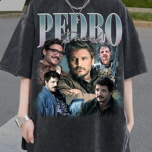 Peut inclure: T-shirt gris foncé avec un collage d'images de Pedro Pascal, avec le nom "PEDRO Pascal" dans une police dégradée. Le t-shirt a un aspect vintage et vieilli, avec une apparence délavée.