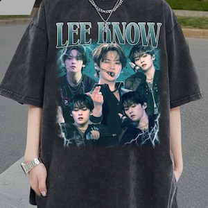 May include: Dark gray oversized t-shirt featuring a graphic of a musical group with the text "LEE KNOW" in a teal font. The shirt has a vintage, worn look.