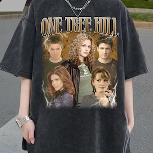 May include: Dark gray t-shirt featuring the text "ONE TREE HILL" above a collage of six people. The shirt has a vintage, distressed look. The text "TAAJIRBILLAH" is in the upper left corner.