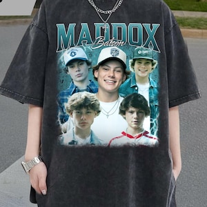 May include: Dark gray t-shirt featuring a graphic of five young men with the name "MADDOX Batson" in teal lettering. The shirt has a vintage, faded appearance and a relaxed fit.