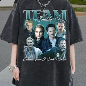 Op de afbeelding: Donkergrijze oversized t-shirt met een afbeelding van meerdere mannen, de tekst "TEAM Daddy" en "Charlie Swan & Carlisle Cullen". Het shirt heeft een vintage, vervaagde uitstraling.