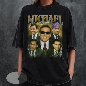 May include: Black t-shirt featuring a collage of images of Michael Scott from The Office, with the name "MICHAEL" in gold lettering. The design includes various expressions and outfits of the character, with lightning bolt accents.