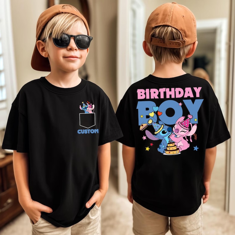 May include: Black t-shirt with a pocket design featuring a cartoon character and the word "CUSTOM" in blue. The back of the shirt has the words "BIRTHDAY BOY" and a cartoon character design. The shirt is worn by a child.