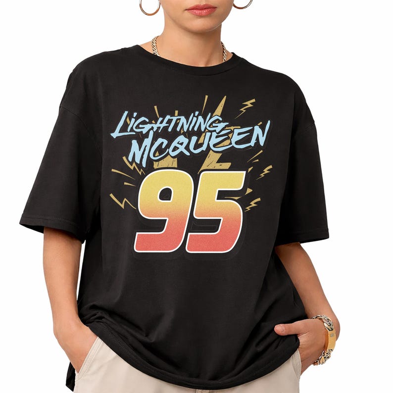 May include: A black short-sleeved t-shirt featuring the text Lightning McQueen in light blue letters above a large number 95 in a yellow-to-red gradient. The design includes yellow lightning bolt graphics surrounding the text and number.