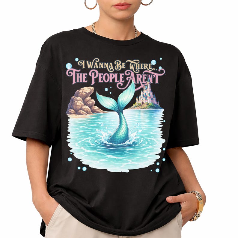 K&ouml;nnte beinhalten: Ein schwarzes T-Shirt mit einem Grafikdruck, der eine t&uuml;rkisfarbene Meerjungfrauenflosse zeigt, die in blaues Wasser eintaucht, mit felsigem Ufer, einem Schloss in der Ferne und dem Text "I WANNA BE WHERE THE PEOPLE AREN'T" in dekorativer Schrift.