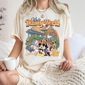 Pode incluir: Uma t-shirt de cor creme com uma impress&atilde;o gr&aacute;fica do Walt Disney World com o Mickey Mouse, a Minnie Mouse, o Pato Donald, a Margarida, o Pateta e o Pluto. O design inclui o castelo ic&oacute;nico, um monotrilho e o texto Walt Disney World.