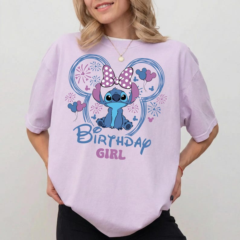 May include: A light purple t-shirt featuring a cartoon character with a polka dot bow, surrounded by fireworks and balloons. The text "Birthday Girl" is printed below the character in blue and pink.