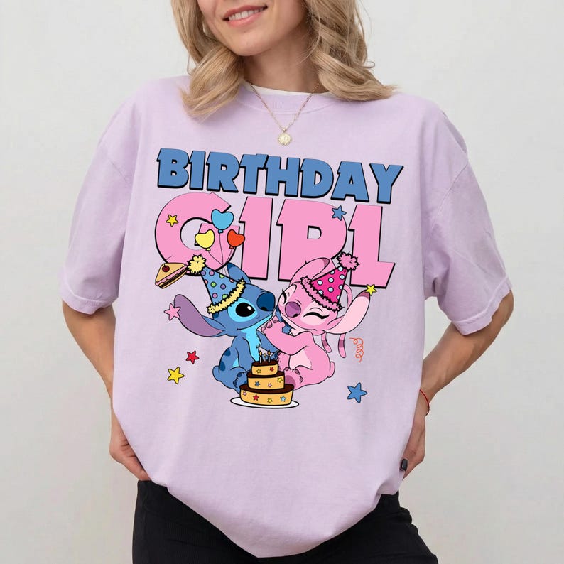 May include: A light purple t-shirt featuring the words "BIRTHDAY GIRL" in blue and pink. The graphic includes cartoon characters Stitch and Angel, with a birthday cake and party hats. Stars and hearts decorate the design.