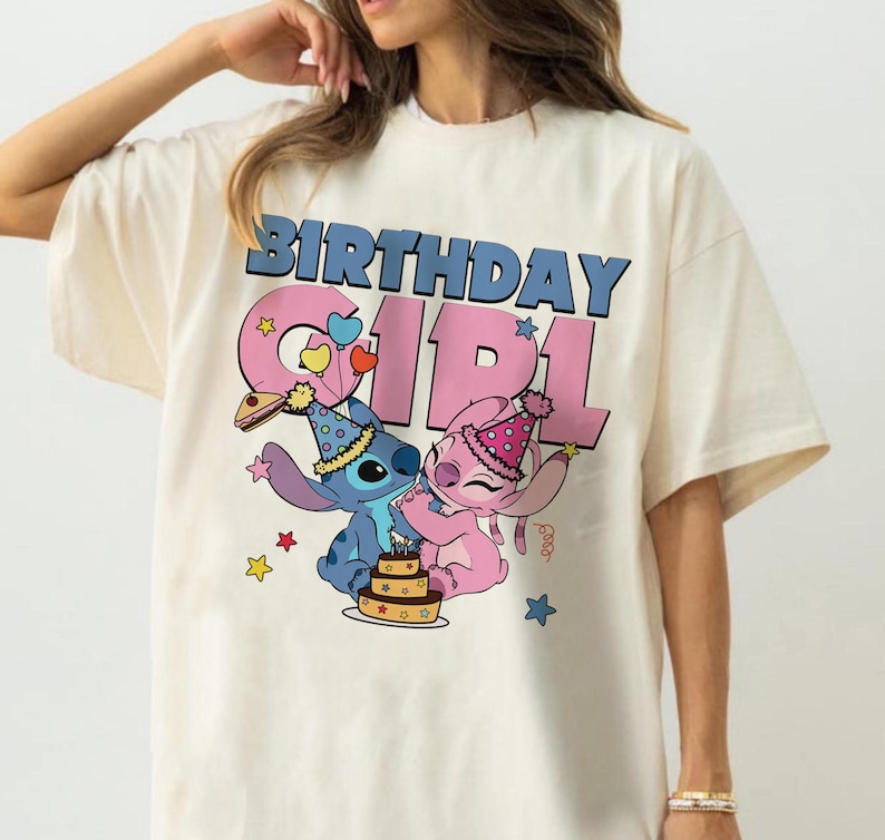 May include: Cream-colored t-shirt featuring the text "BIRTHDAY GIRL" in blue and pink. The graphic includes cartoon characters Stitch and Angel, a birthday cake, and star and heart accents. The shirt has short sleeves.