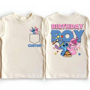 May include: Cream-colored t-shirt featuring a cartoon graphic of two characters wearing party hats, with the text "BIRTHDAY BOY" on the back. The front has a pocket design with the word "CUSTOM".