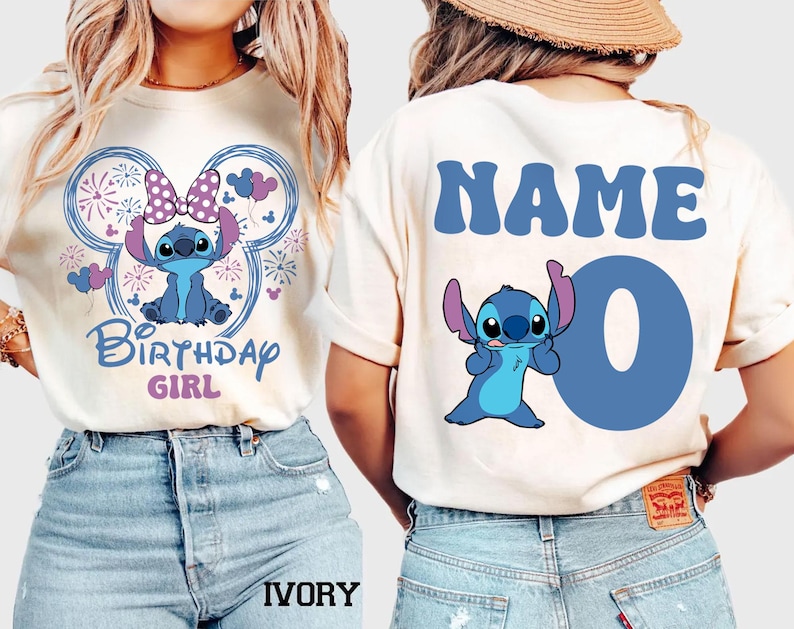 May include: Ivory-colored t-shirt featuring a blue cartoon character with a bow, surrounded by a Mickey Mouse-shaped design with fireworks and the text "Birthday Girl." The back of the shirt has the word "NAME" and the number "0".