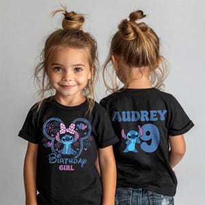 May include: Two young girls wearing black t-shirts with a Stitch-themed design. The front of the shirt features Stitch, a bow, and the words "Birthday Girl." The back of the shirt has the name "Audrey" and the number "9."