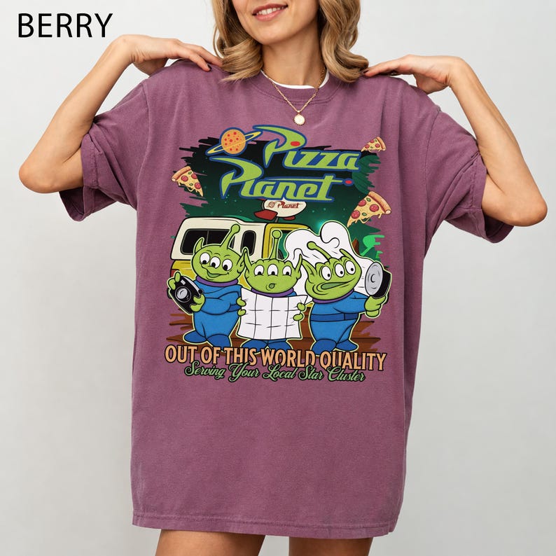 May include: A berry-colored short-sleeve t-shirt featuring a graphic print of three green aliens from Pizza Planet. The design includes the text Pizza Planet, Out of This World Quality, and Serving Your Local Star Cluster with pizza slices.