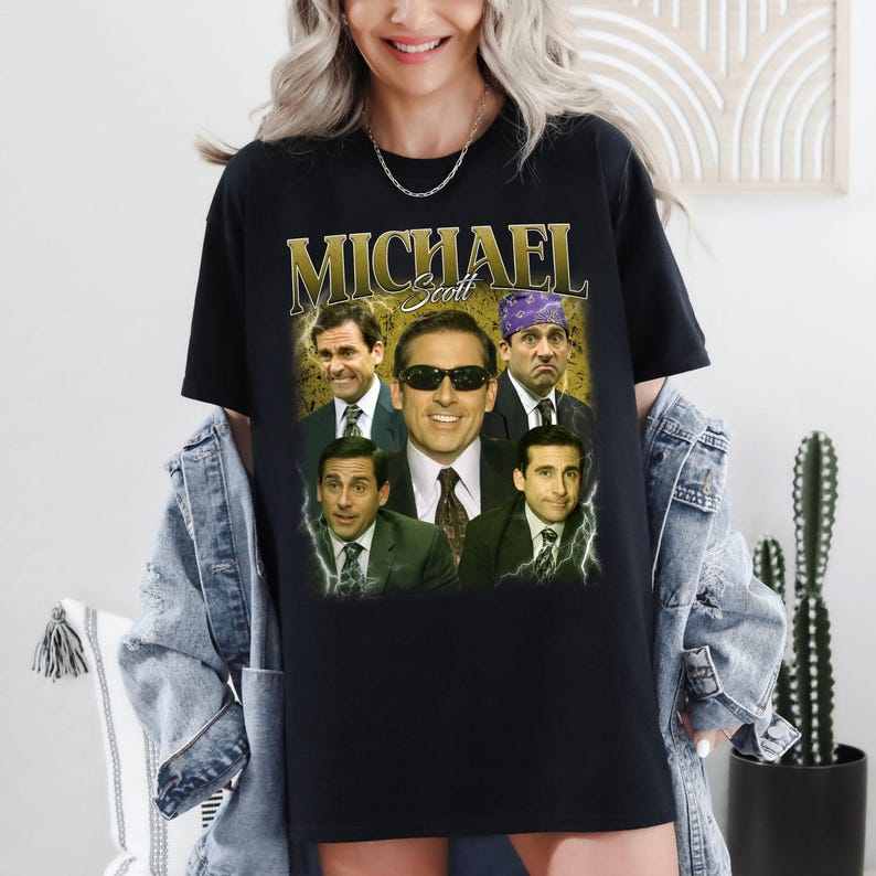 May include: Black t-shirt featuring a graphic of Michael Scott from The Office. The design includes multiple images of the character with the name "MICHAEL Scott" in gold lettering. The shirt is a classic crew neck style.