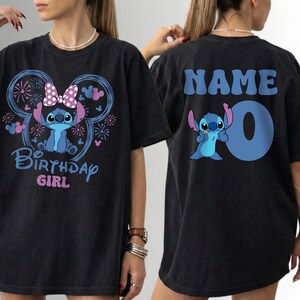 May include: Black t-shirt featuring a blue cartoon character with a bow and the text "Birthday Girl" on the front. The back of the shirt has the word "NAME" and the number "0" with the same cartoon character.