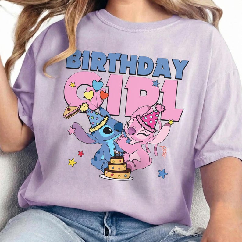 May include: A light purple t-shirt featuring a graphic of the characters Stitch and Angel from Lilo & Stitch. The text "BIRTHDAY GIRL" is in blue and pink. The characters are celebrating with a cake and party hats.