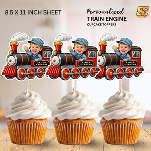 May include: Three cupcakes topped with white frosting, each adorned with a personalized train engine cupcake topper. The toppers feature a smiling child in a conductor's hat, with the text "JAMES EXPRESS". The sheet size is 8.5 x 11 inches.