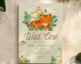 May include: A light green invitation card with a cartoon tiger illustration. The text "Wild One" is displayed in a cursive font, with additional text below announcing a first birthday party. Floral and leaf accents surround the text and illustration.