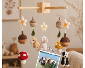 Op de afbeelding: Een handgemaakte houten baby mobile met gehaakte elementen. De mobiel bevat witte bloemen, eikels, bladeren, paddenstoelen en hondenfiguren in verschillende kleuren. Een foto van drie honden in het water is ook inbegrepen.