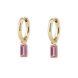 May include: A pair of gold hoop earrings with a rectangular pink gemstone pendant. The earrings are displayed against a white background, highlighting the jewelry's design and color. The earrings are a classic and elegant accessory.