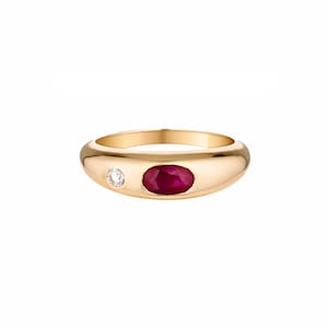 Puede incluir: Un anillo de oro con un gran rubí ovalado y un pequeño diamante. El anillo tiene una banda lisa y redondeada y un acabado pulido. El rubí es de color rojo intenso y el diamante es transparente. Joyería.