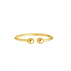 May include: A minimalist gold ring with a simple design. The ring features a thin band that curves around to meet two small, round, gold spheres. The ring is set against a white background.