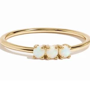 Op de afbeelding: Een delicate gouden ring met drie ovale, witte opaal edelstenen in een rij. De ring heeft een dunne band en een gepolijste afwerking. De edelstenen zijn het middelpunt van de ring.