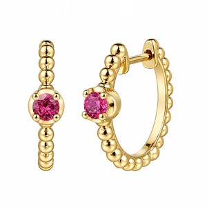 Könnte beinhalten: Ein Paar goldene Creolen mit einem leuchtend pinkfarbenen Edelstein in der Mitte. Die Ohrringe haben ein Perlendesign um den Reifen und entlang des Stifts.