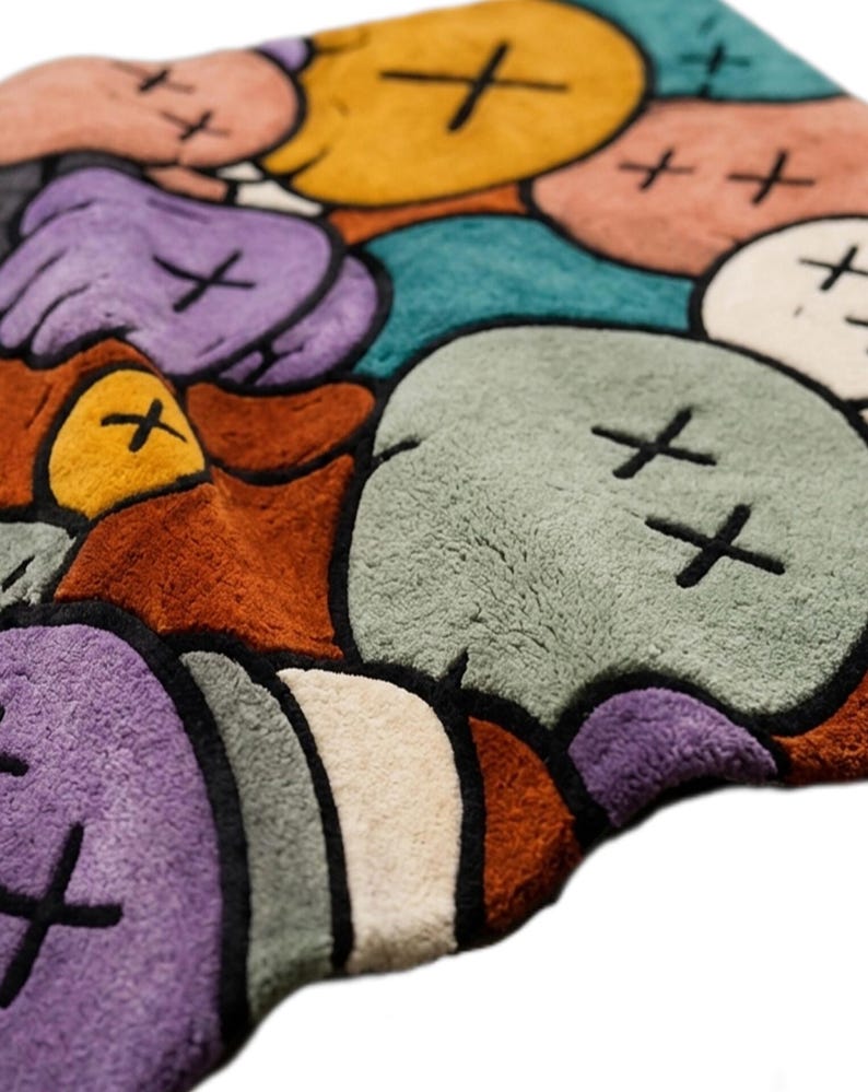 Puede incluir: Una alfombra de felpa con un patr&oacute;n repetitivo de cabezas de personajes redondeadas tipo dibujos animados en tonos amarillo, morado, verde azulado, verde claro, naranja y crema. Cada cabeza est&aacute; delineada en negro con dos X negras.