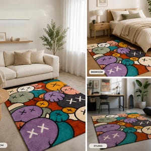 Puede incluir: Una alfombra rectangular con un patr&oacute;n repetitivo de rostros estilo caricatura con ojos en forma de X en tonos vibrantes de morado, azul verdoso, naranja y crema, sobre un fondo rojo intenso, mostrada en tres configuraciones de habitaci&oacute;n.