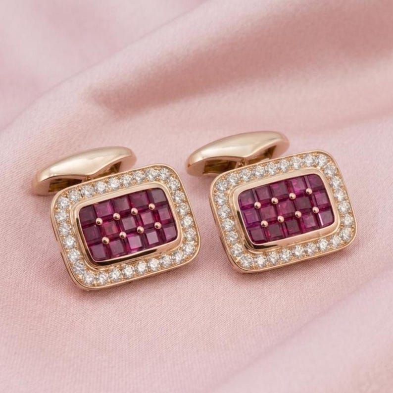 May include: A pair of rectangular cufflinks crafted from rose gold, each featuring a central grid of deep red square-cut rubies surrounded by a border of small, clear, round-cut diamonds, set in a polished metal frame with a hinged toggle back.