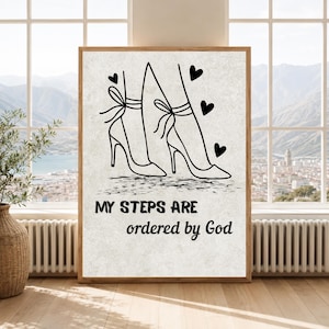 May include: A rectangular wall art print on a light textured background featuring a black line drawing of two high-heeled shoes with ribbon ankle ties and three small hearts. The text reads: MY STEPS ARE ordered by God in black lettering.