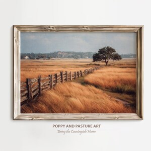 May include: A framed landscape print depicting a rural scene with a wooden fence leading through a field of golden grass. A solitary tree is in the distance under a cloudy sky. The text "POPPY AND PASTURE ART" is visible.