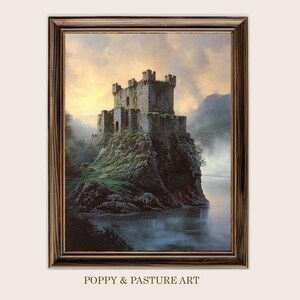 Pode incluir: Uma impressão emoldurada de um castelo de pedra numa ilha rochosa, rodeado por água e névoa. O castelo tem várias torres. A obra de arte é emoldurada em madeira escura, com um céu nublado.