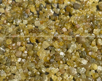 Puede incluir: Primer plano de un montón de diamantes en bruto. Las piedras preciosas muestran una gama de colores, incluyendo amarillo, dorado y marrón. La imagen muestra el estado natural, sin cortar, de los diamantes, con sus estructuras cristalinas y texturas variadas.