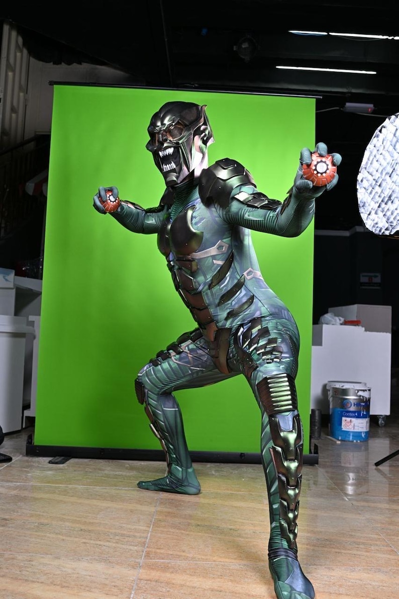 May include: A Green Goblin costume with a detailed mask and armor-like accents. The costume features a green and black color scheme, with intricate patterns and designs. The character is holding two orange and red devices.