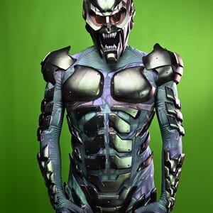 May include: A detailed costume of the Green Goblin, featuring a metallic helmet with menacing eyes and a jagged mouth. The suit has armored plating and is holding two red, spherical grenades. The background is a solid green.