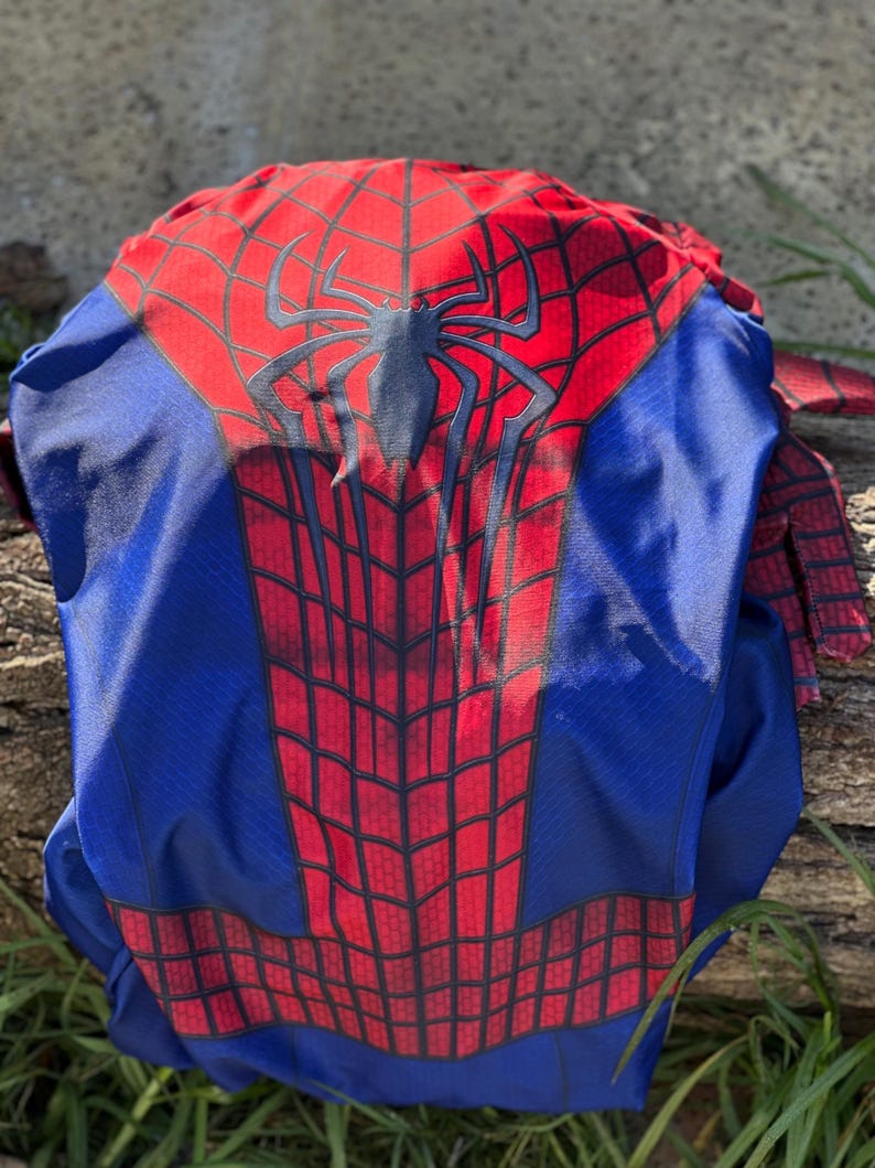 Może przedstawiać: Niebiesko-czerwony kostium Spider-Mana. Kostium ma czerwony wz&oacute;r pajęczyny na klatce piersiowej i plecach, z dużym czarnym emblematem pająka. Ramiona i rękawy są czerwone, a reszta kostiumu jest niebieska.