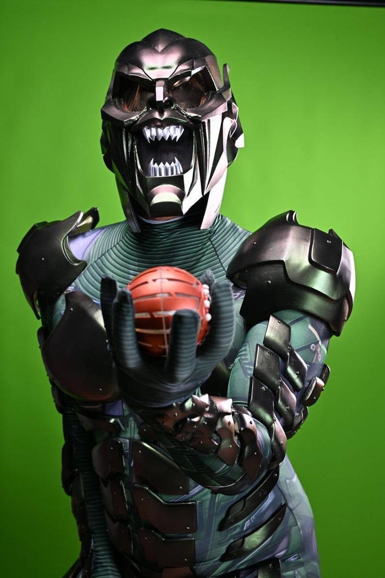 May include: A detailed costume of the Green Goblin, featuring a metallic mask with a menacing grin and sharp teeth. The costume includes a green and black armored suit, with the character holding a red pumpkin bomb.
