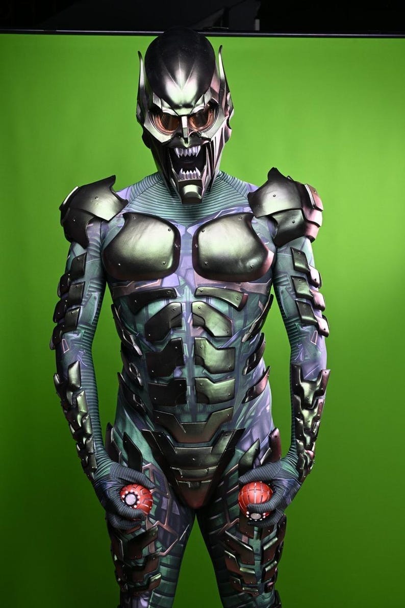 May include: A full-body costume featuring a metallic green and purple design. The costume includes a detailed helmet with a menacing expression and red-tinted lenses. The suit has armored plating and is holding two red, spherical objects.
