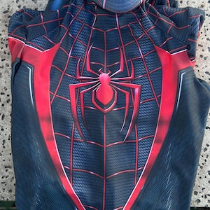 May include: A black and red Spider-Man costume with a hood. The costume features a spider web design with a large spider emblem on the chest. Red accents outline the design, creating a striking visual.
