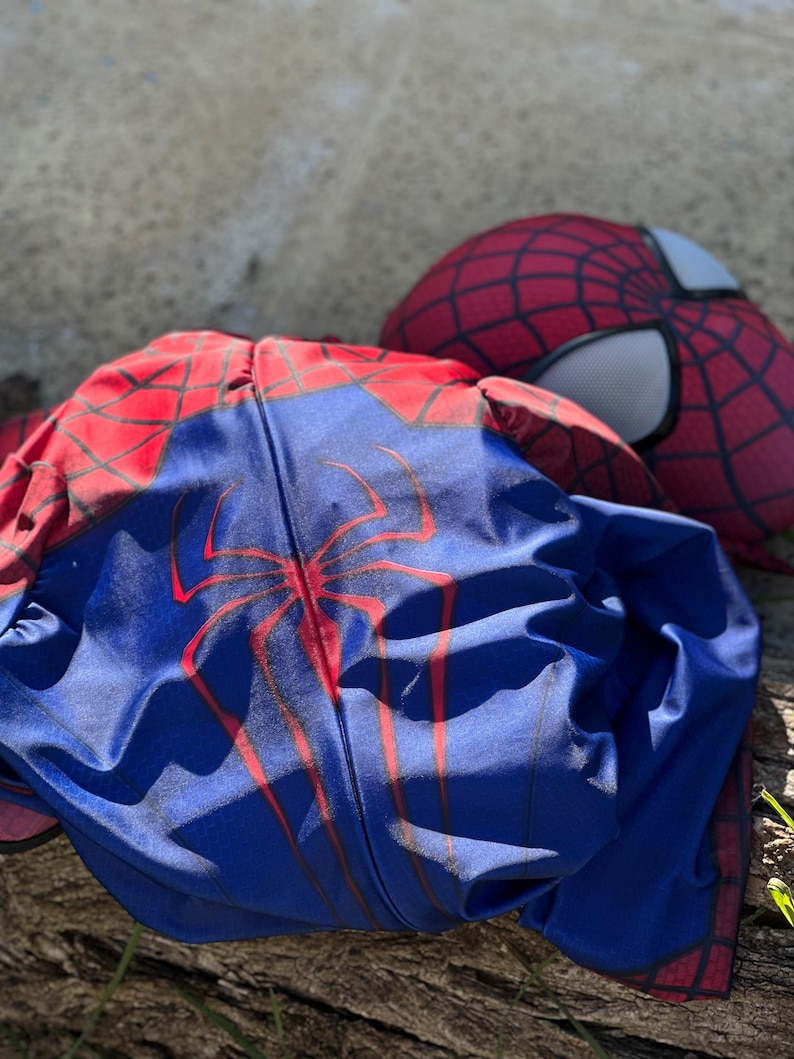 Może przedstawiać: Niebiesko-czerwony kostium Spider-Mana z pasującą maską. Kostium ma duży czerwony emblemat pająka na klatce piersiowej i czerwone wzory pajęczyny. Maska ma białe osłony oczu i czerwony wz&oacute;r pajęczyny.