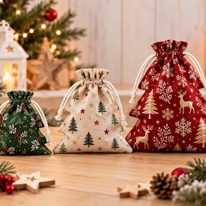 Può includere: Tre sacchetti in tessuto a forma di albero con coulisse, nei colori verde, crema e rosso. Il sacchetto verde presenta foglie bianche e rosse, quello crema alberi verdi e stelle rosse, quello rosso renne, fiocchi di neve e alberi dorati.