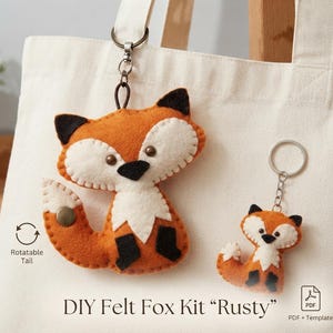 Könnte beinhalten: Ein DIY-Filz-Fuchs-Set namens Rusty mit zwei orangefarbenen, weißen und schwarzen fuchsartigen Filzornamenten mit genähten Details, dunklen Augen und einem drehbaren Schwanzmechanismus. Das Set enthält eine PDF-Vorlage für diese Fuchsschlüsselanhänger.